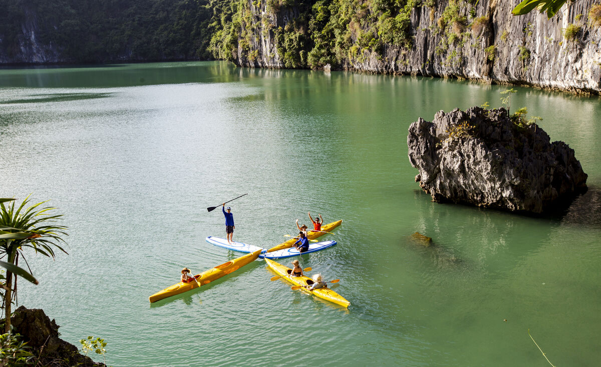 Group of kayakers paddling between limestone cliffs in Lan Ha Bay